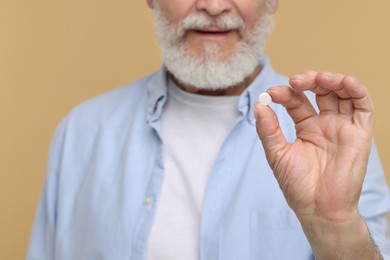 Photo of Senior man with pill on beige background, closeup