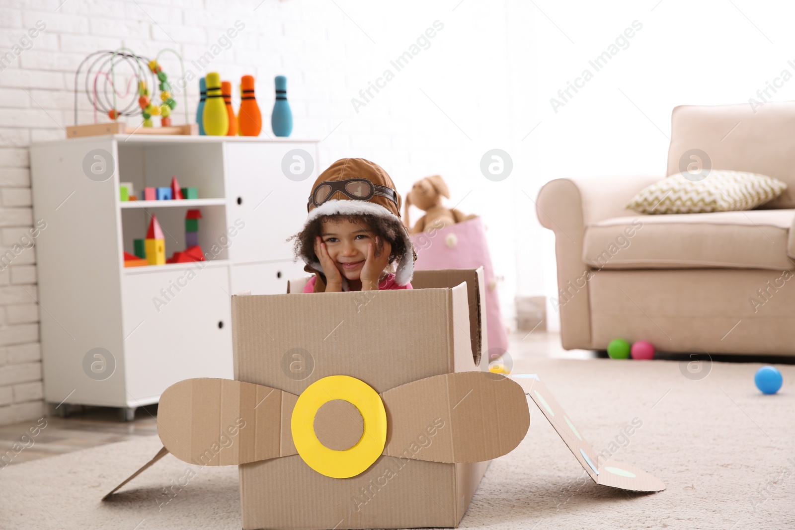 Photo of Cute African American child playing with cardboard plane at home