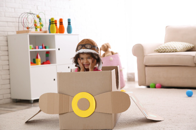 Cute African American child playing with cardboard plane at home