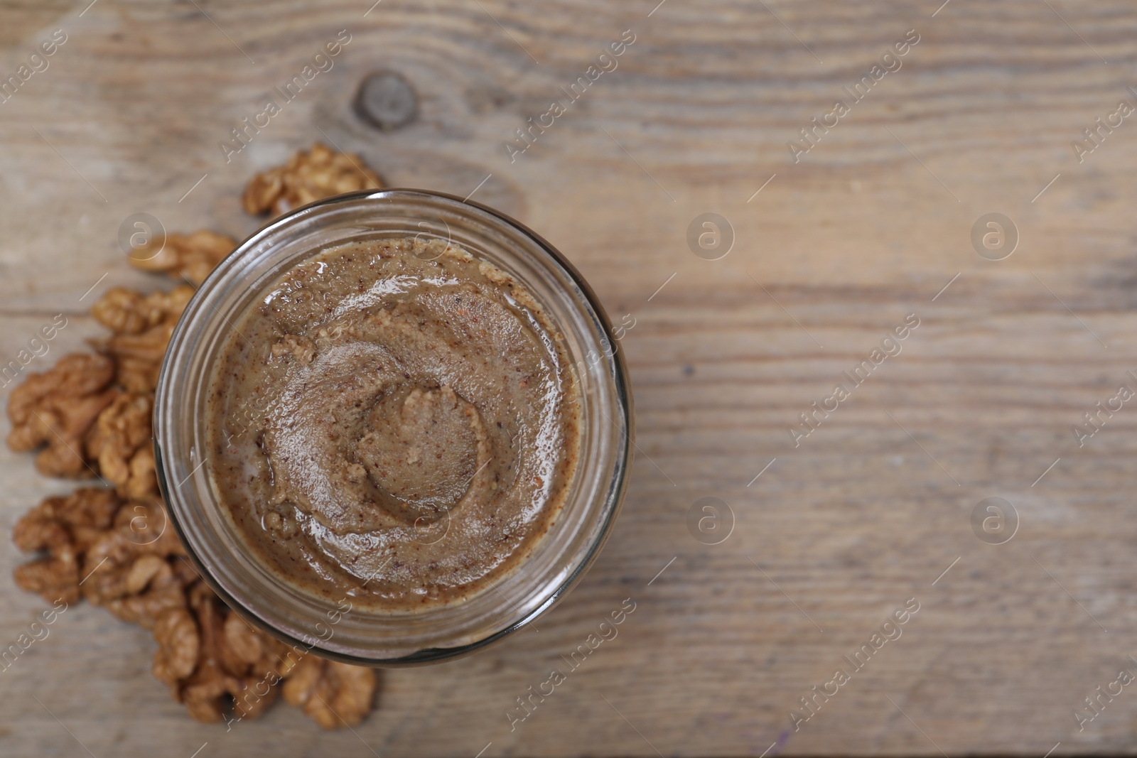 Photo of Tasty walnut nut paste in jar on wooden table, top view. Space for text