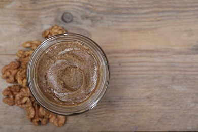 Tasty walnut nut paste in jar on wooden table, top view. Space for text