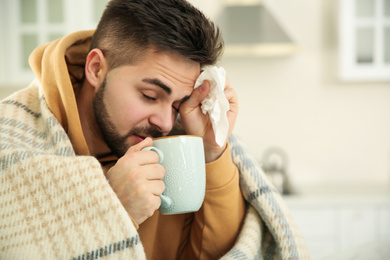 Photo of Sick young man with cup of hot drink and tissue at home. Influenza virus