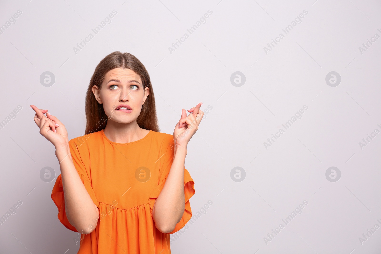 Photo of Portrait of hopeful young woman with crossed fingers on white background