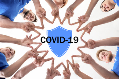 Image of Volunteers uniting to help during COVID-19 outbreak. Group of people holding hands together, shield illustration