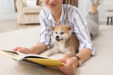Young woman reading book with cute dog on floor in living room, closeup