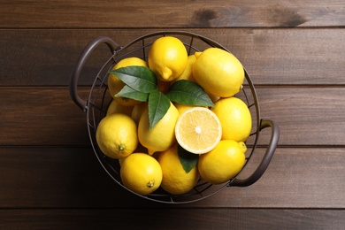 Many fresh ripe lemons with green leaves on wooden table, top view