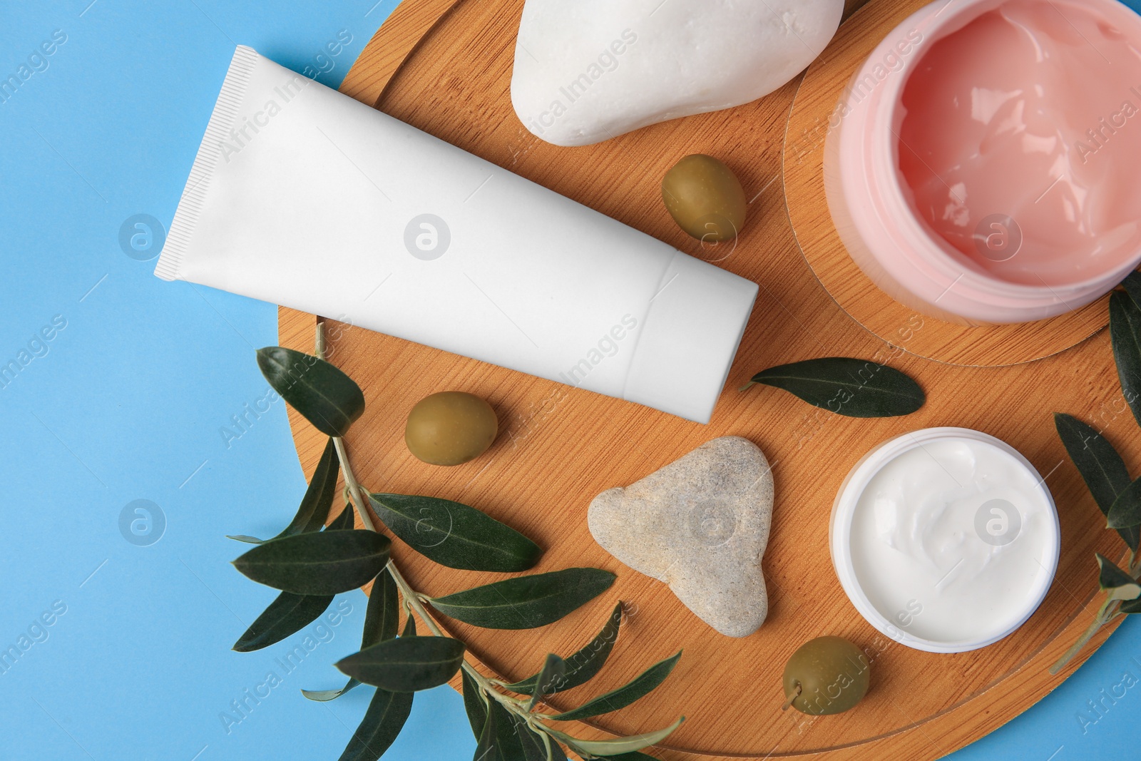 Photo of Different cosmetic products with olives and stones on light blue background, top view