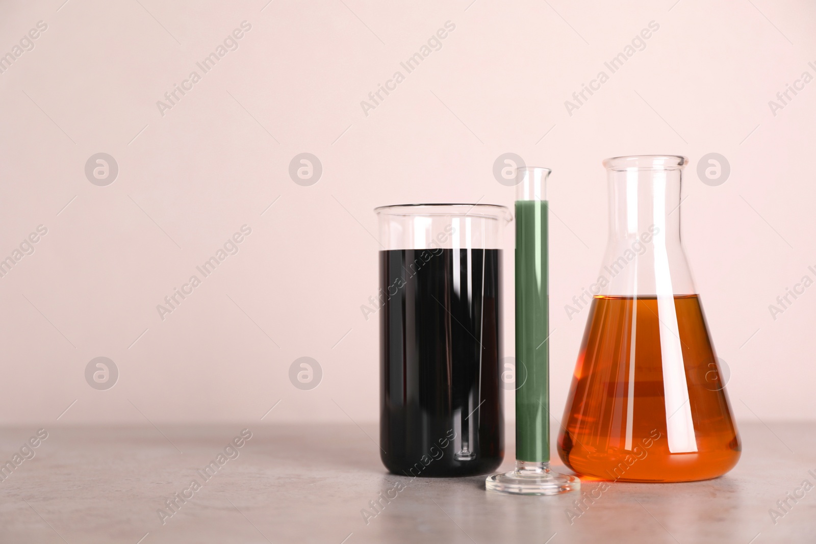 Photo of Test tube, beaker and flask with different types of oil on grey table against light background, space for text