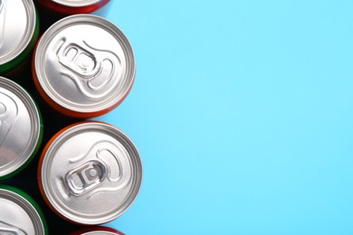 Photo of Energy drink in cans on light blue background, top view. Space for text