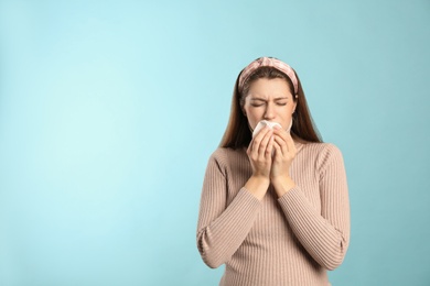 Photo of Young woman with tissue suffering from runny nose on light blue background. Space for text