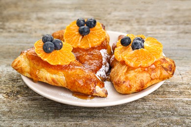 Fresh tasty puff pastry with sugar powder, jam, tangerines and blueberries on wooden table, closeup