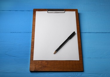 Photo of Clipboard with sheet of paper and pen on light blue wooden table. Space for text