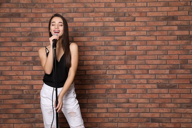 Photo of Young stylish woman singing in microphone near brick wall. Space for text