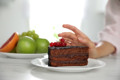 Photo of Woman choosing between sweets and healthy food at white table, closeup