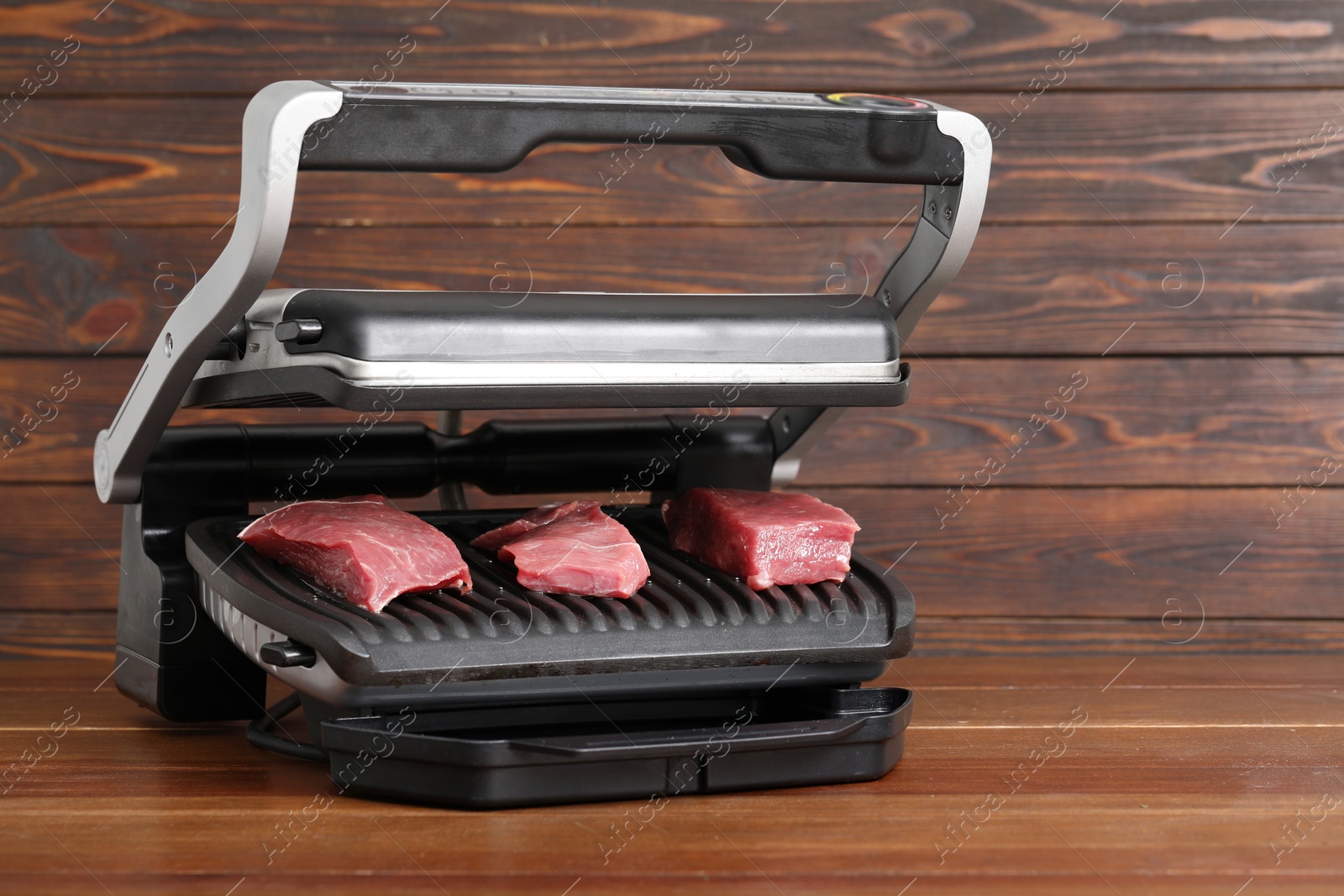 Photo of Electric grill with raw meat on wooden table. Space for text