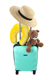 Photo of Soft travel pillow, toy bear and hat on turquoise suitcase isolated on white