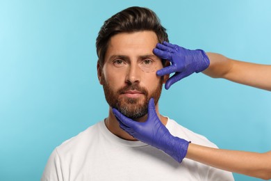 Photo of Doctor checking patient's face before cosmetic surgery operation on light blue background