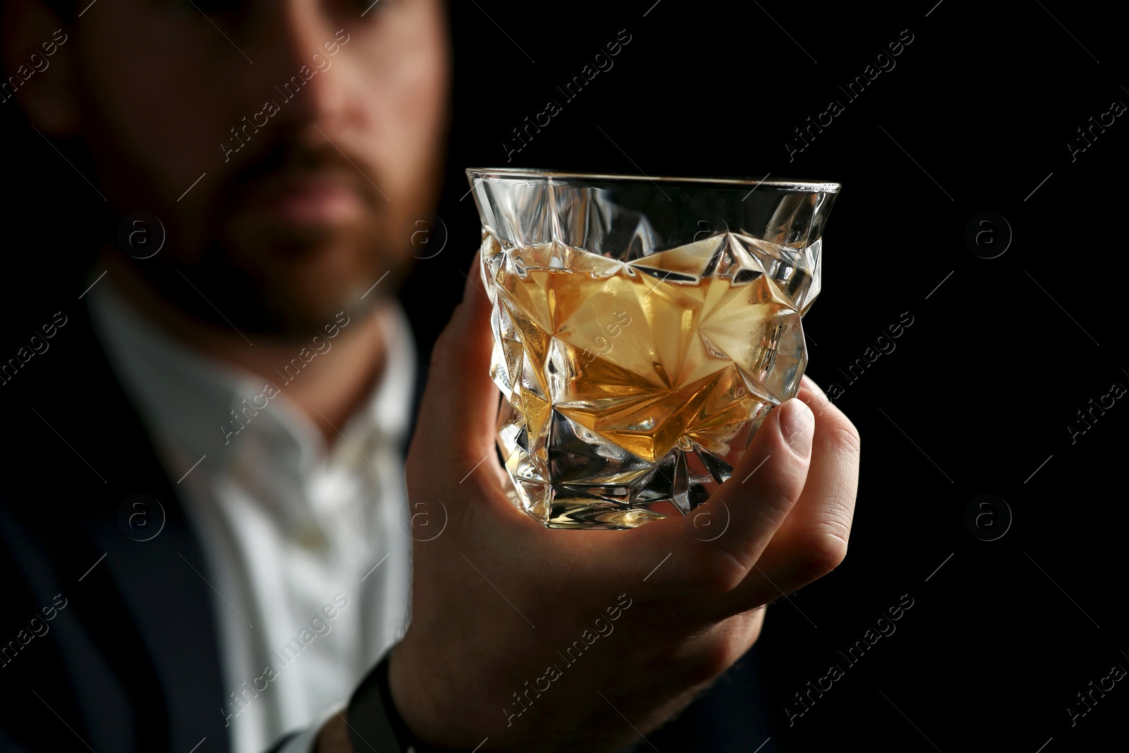 Photo of Man holding glass of whiskey with ice cubes on black background, selective focus