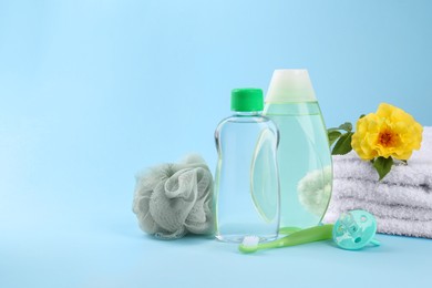 Photo of Bottles with baby oil, flower and accessories on light blue background, space for text