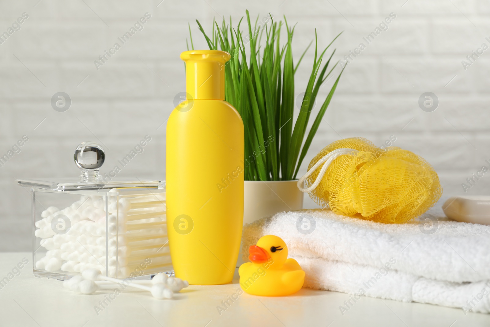 Photo of Baby cosmetic product, bath duck, cotton swabs and towel on white table against brick wall