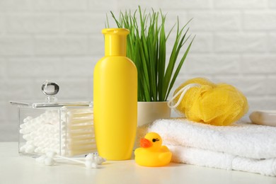 Baby cosmetic product, bath duck, cotton swabs and towel on white table against brick wall