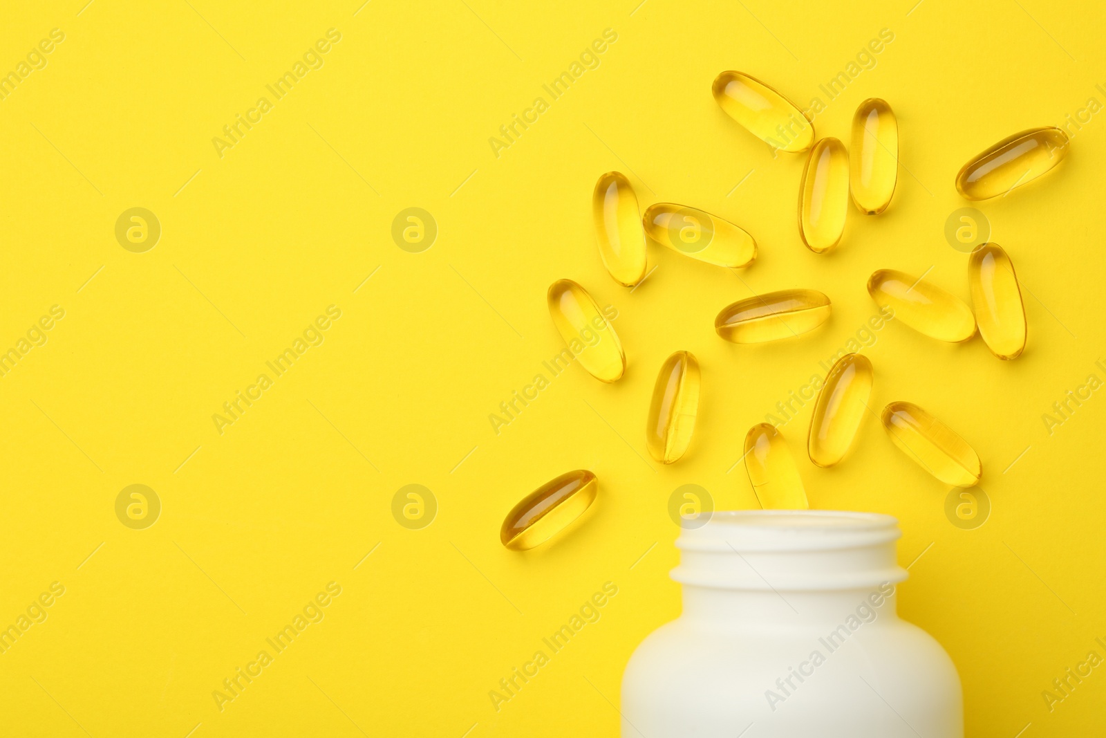 Photo of Softgel capsules and bottle on yellow background, top view. Space for text