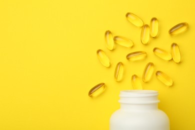 Softgel capsules and bottle on yellow background, top view. Space for text