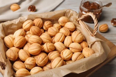 Photo of Wicker basket of delicious nut shaped cookies with boiled condensed milk on light wooden table, closeup