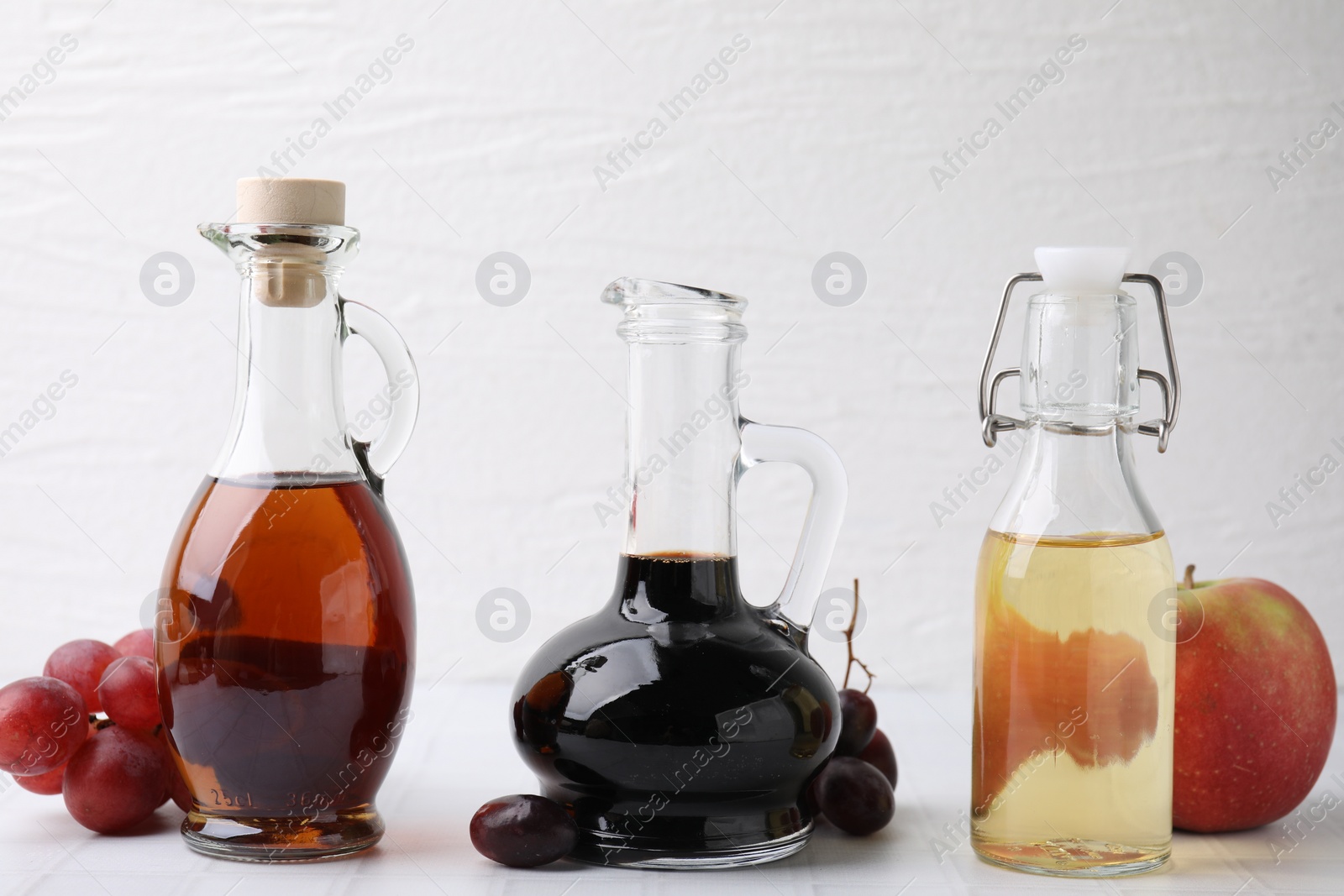 Photo of Different types of vinegar and ingredients on light tiled table, closeup