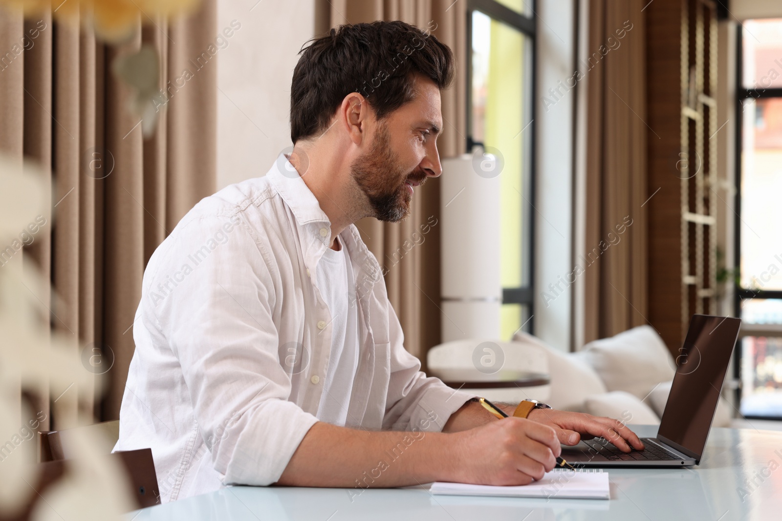 Photo of Man working on laptop and writing something at table in cafe