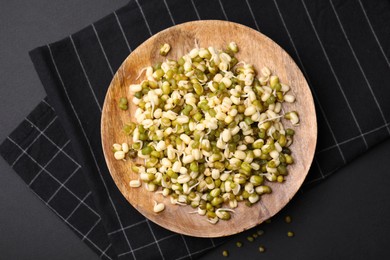 Photo of Wooden plate with sprouted green mung beans on black background, flat lay