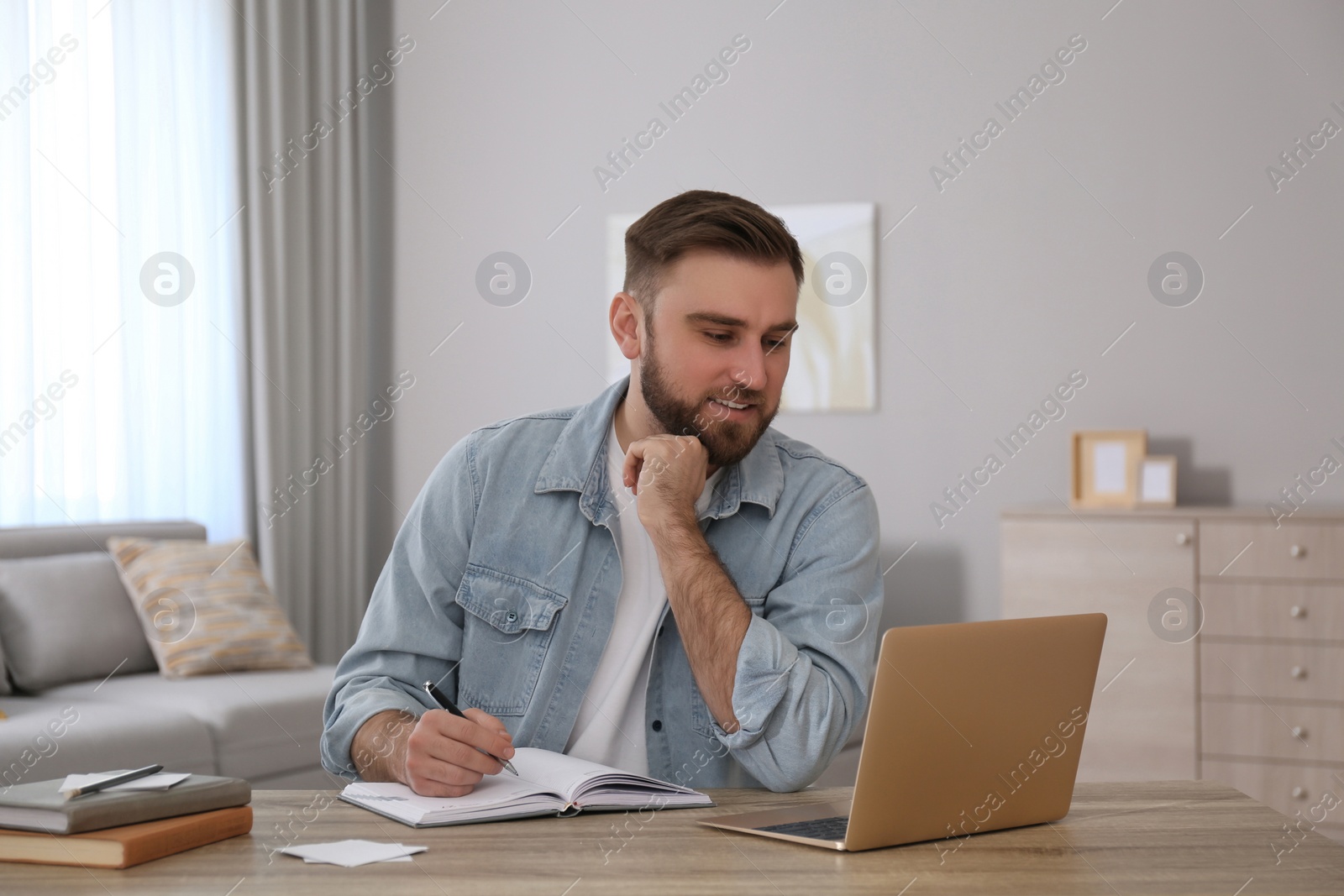 Photo of Young man taking notes during online webinar at table indoors