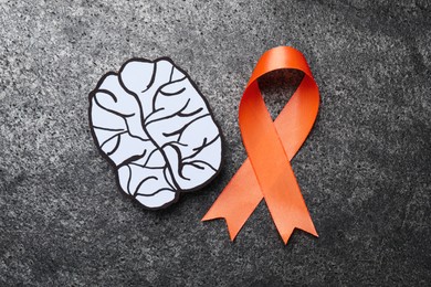 Photo of Orange ribbon and paper brain cutout on grey table, flat lay. Multiple sclerosis awareness