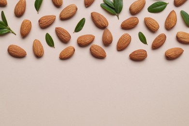 Delicious almonds and fresh leaves on beige background, flat lay. Space for text