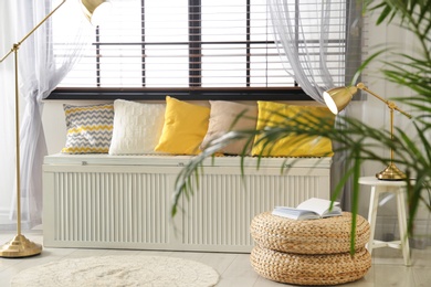 Photo of Wooden chest with pillows near window in room. Interior design