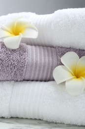 Photo of Stack of folded terry towels and plumeria flowers on table, closeup