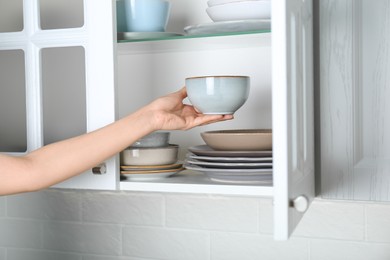 Photo of Woman taking ceramic bowl from cabinet at home, closeup