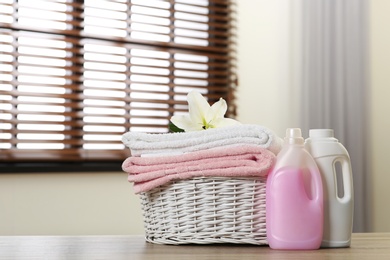 Photo of Clean towels with lily in basket and detergents on table indoors. Space for text