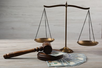 Photo of Judge's gavel, money and scales of justice on wooden table