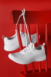 Photo of Stylish sneakers with white shoe laces hanging on chair against red background