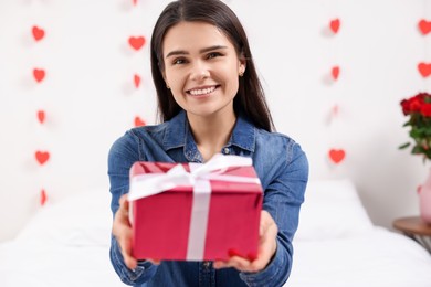 Photo of Beautiful young woman with gift box indoors, view from camera. Valentine's day celebration in long distance relationship