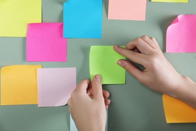 Photo of Woman sticking light green note on grey wall, closeup