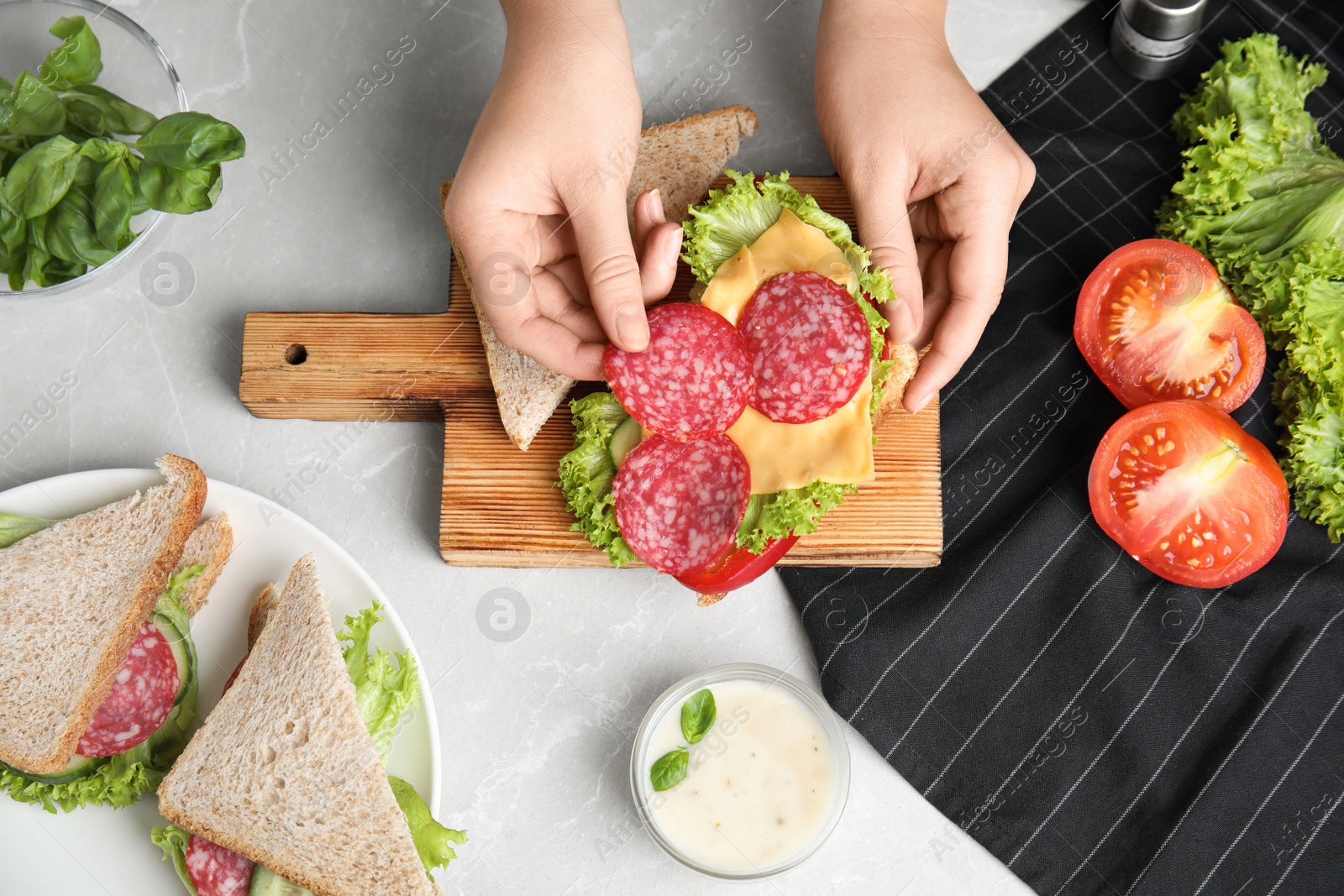 Photo of Woman making tasty sandwich with sausage at light grey marble table, top view