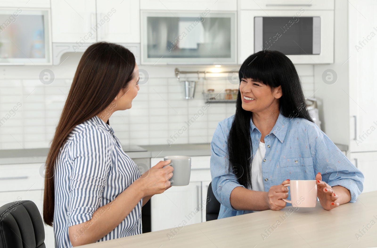 Photo of Young daughter speaking with her mature mother at table indoors