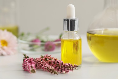 Photo of Bottle of cosmetic oil and flowers on white table in laboratory, closeup