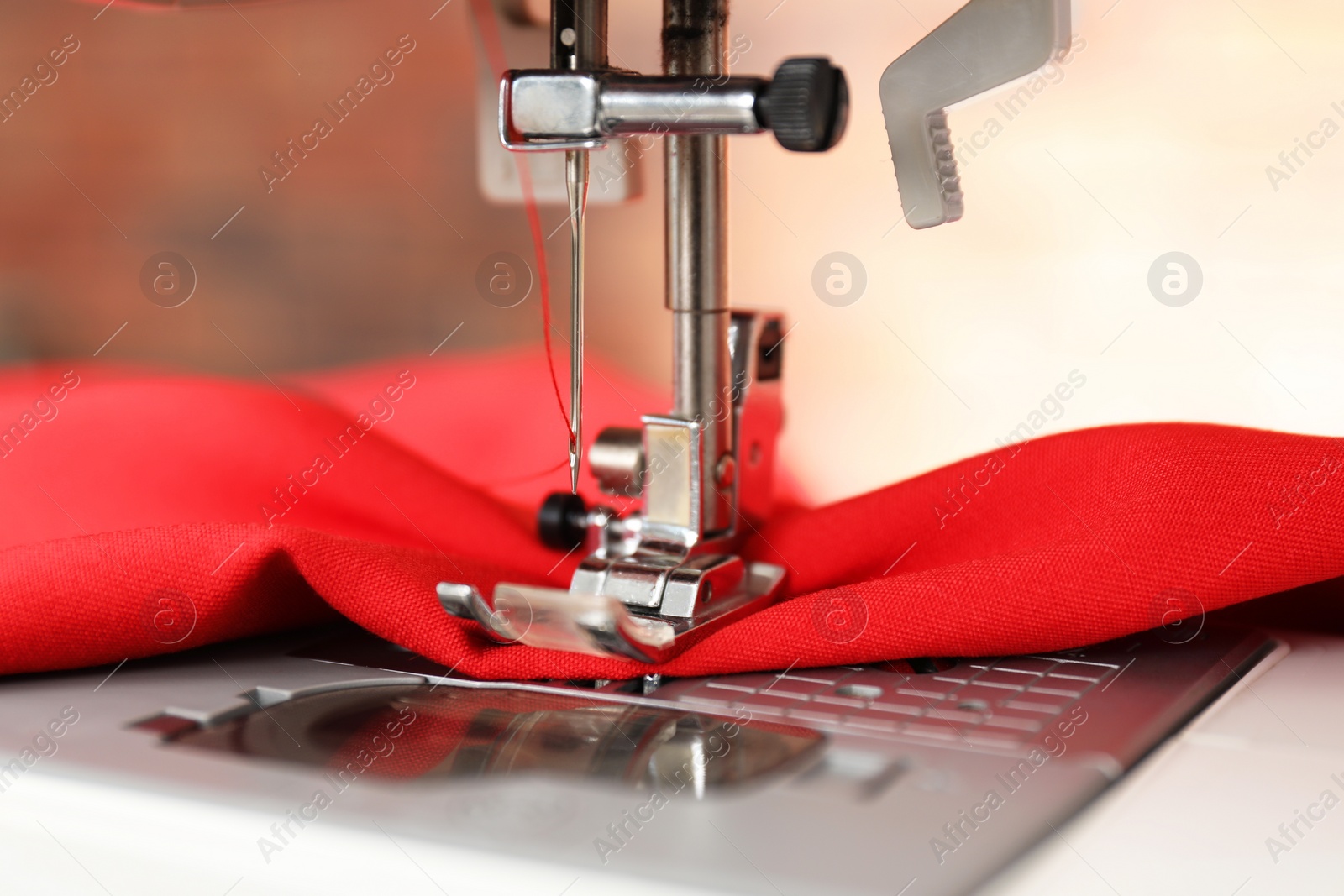 Photo of Sewing machine with red fabric indoors, closeup