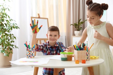 Photo of Little children painting hands at table indoors