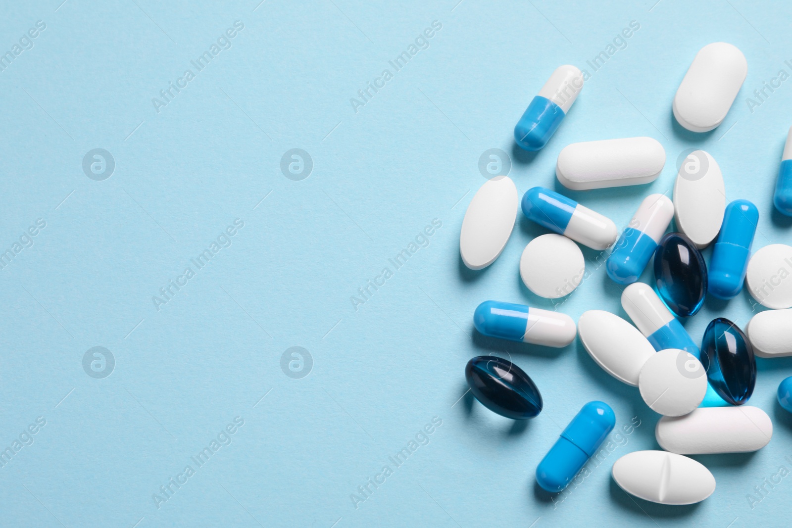 Photo of Many different pills on light blue background, flat lay. Space for text