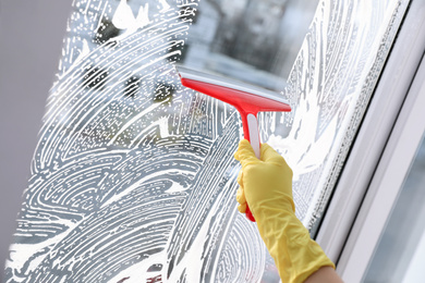 Photo of Woman cleaning window with squeegee indoors, closeup