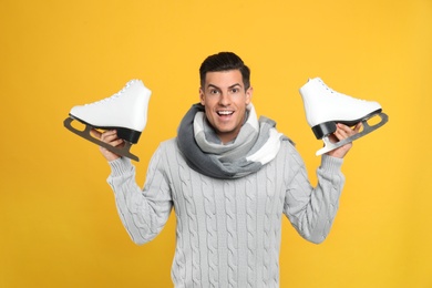 Emotional man with ice skates on yellow background